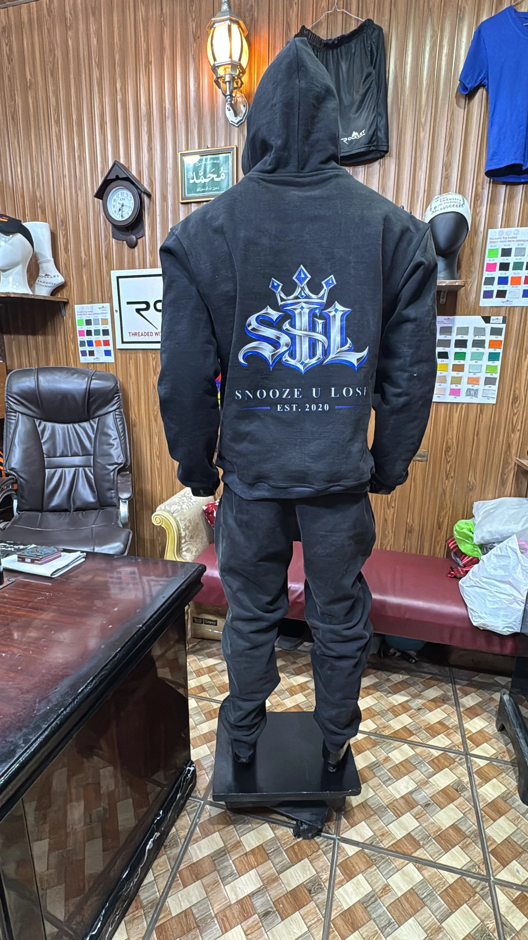 Rear view of a charcoal SUL hoodie sample with a blue and chrome crown logo